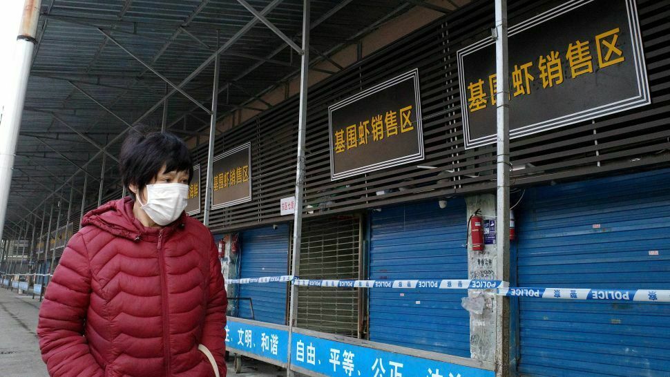 Женщина в маске у закрытого рынка, на котором продавали морепродукты и животных и откуда, как считается, пошел вирус 2019-nCoV